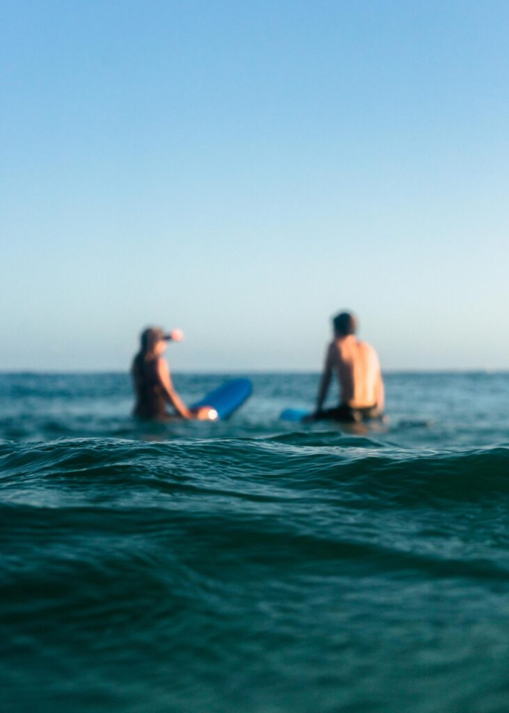 A man and woman enjoy surfing on the ocean waves during a sunny day, showcasing relaxation and leisure.