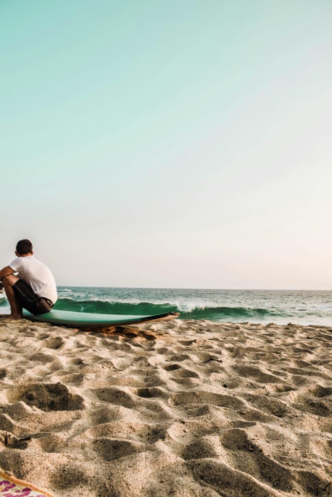 A lone surfer relaxes on a tranquil beach at dusk, enjoying the ocean view.