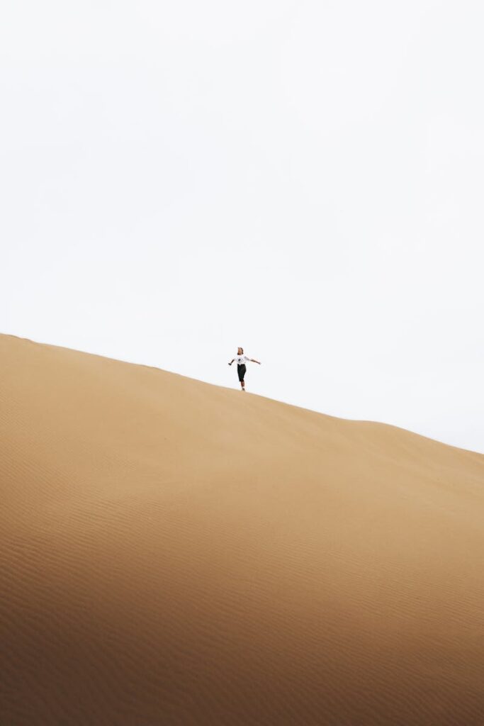 Silhouetted woman running on vast sand dunes under a bright sky in Antalya, Turkey.